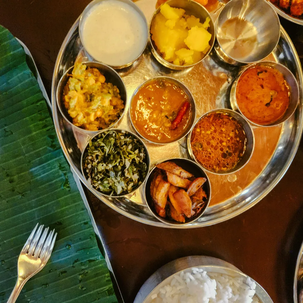 Plateau thali en métal garni de plusieurs petits bols de plats indiens, posé sur une feuille de bananier